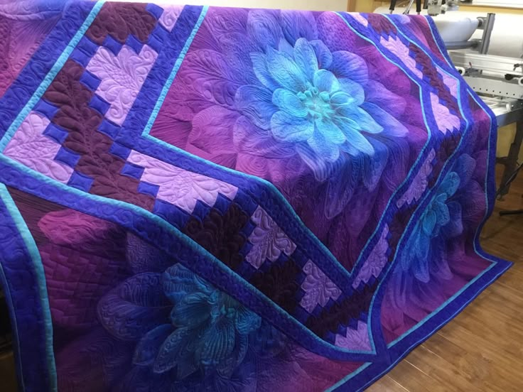 a purple and blue quilt with flowers on it sitting on a table next to an oven