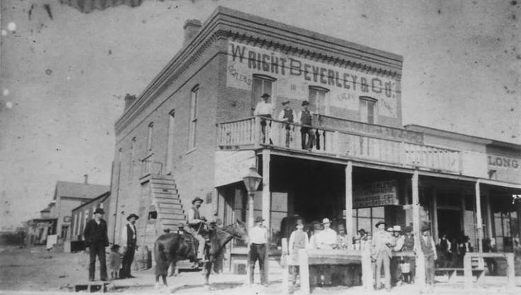 an old black and white photo of men on horses standing in front of a building