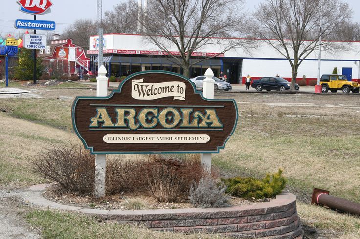 a welcome sign in front of a gas station with cars parked on the lot behind it