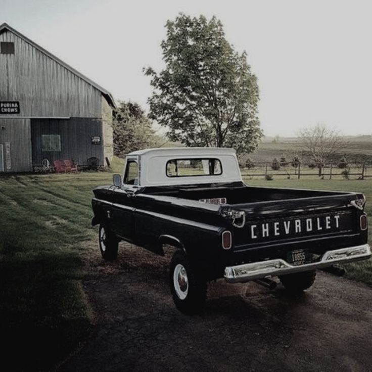 an old black and white chevrolet truck parked in front of a barn with a tree