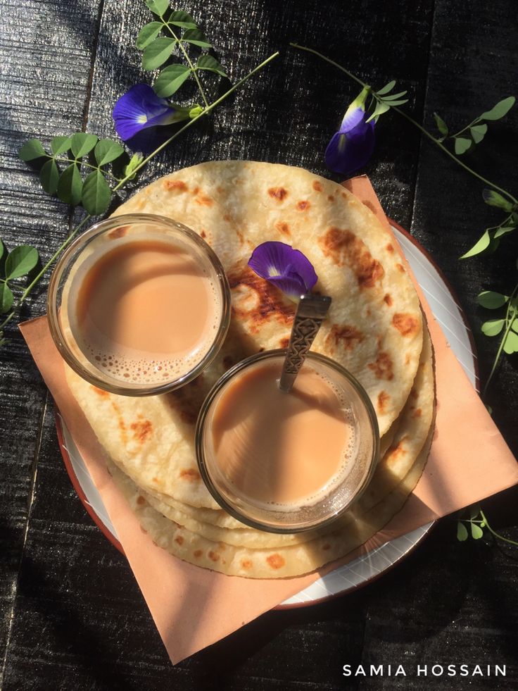 two cups of coffee sit on top of some pita bread with purple flowers in the background