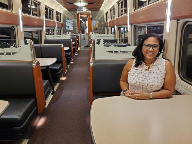 a woman sitting at a table in the middle of a train car with lots of windows