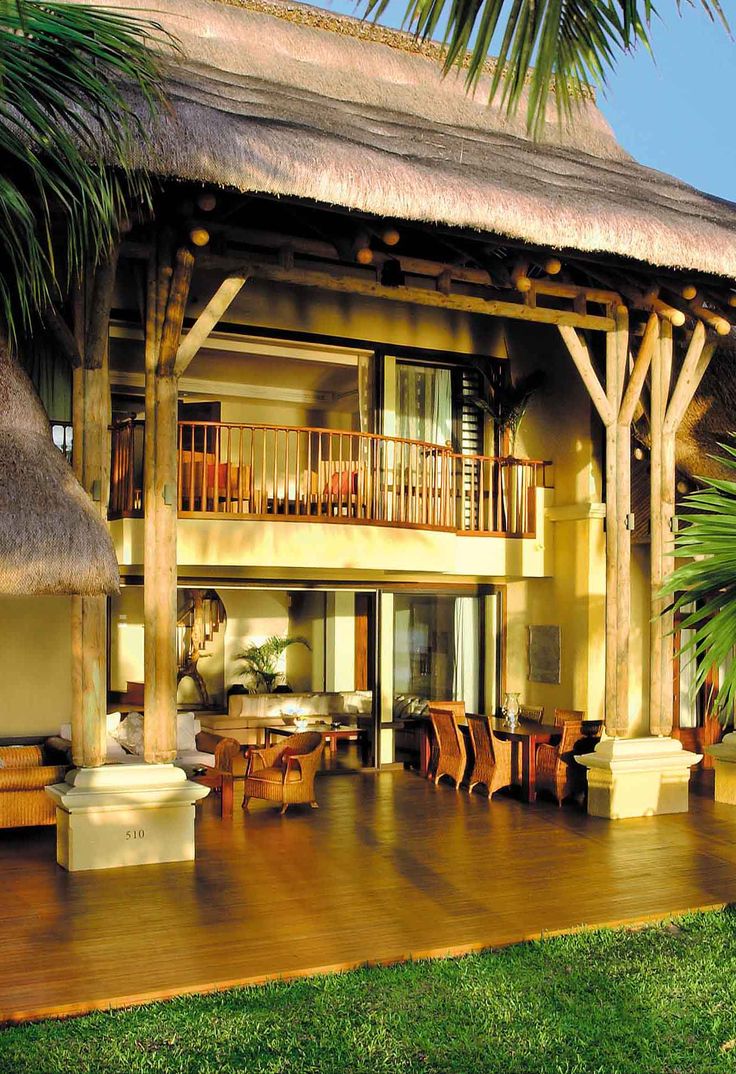 an outside view of a house with wooden furniture and palm trees on the lawn area