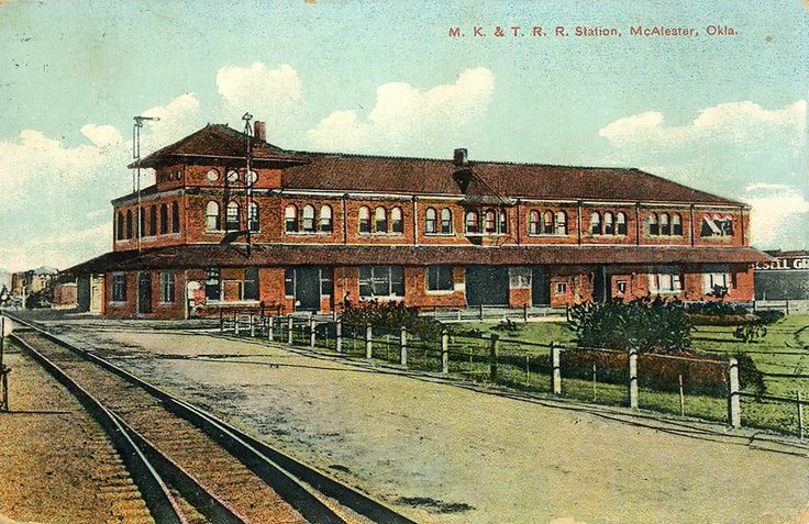 an old photo of a train station with tracks running past it and buildings in the background