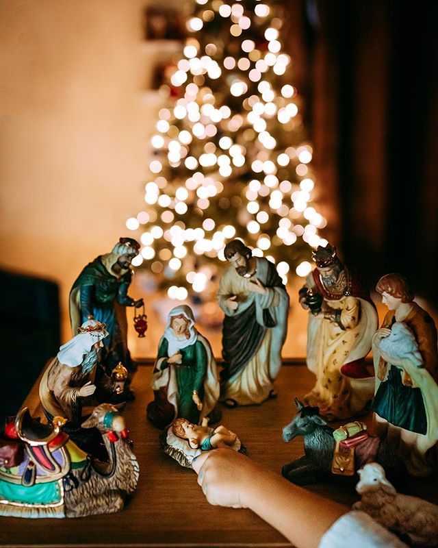 a child's hand reaching for nativity figurines in front of a christmas tree