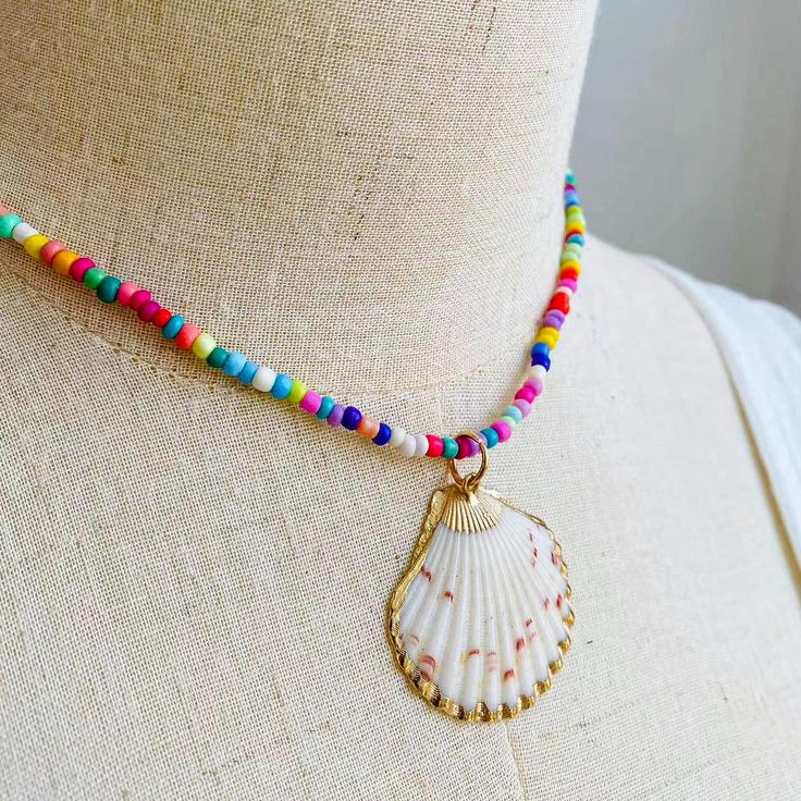 Embrace the essence of summer with this exuberant, colorful beaded necklace, featuring a stunning natural seashell pendant encased in a delicate golden trim. Each bead is meticulously selected to create a kaleidoscope of joy around your neck, reminiscent of a sun-kissed day at the beach or a vibrant festival dance. The heart of this necklace is the seashell pendant, a treasure from the ocean's depths, polished to perfection, and framed in gold. This piece is a celebration of nature's artistry, w Beaded Shell-shaped Jewelry For The Beach, Shell-shaped Beaded Jewelry For Beach Season, Multicolor Shell Jewelry For Vacation, Bohemian Beaded Multicolor Shell, Bohemian Multicolor Beaded Shell, Festival Beaded Shell Necklace In Strand Shape, Summer Beaded Shell Necklaces, Bohemian Shell-shaped Jewelry With Colorful Beads, Multicolor Shell Necklaces For Vacation