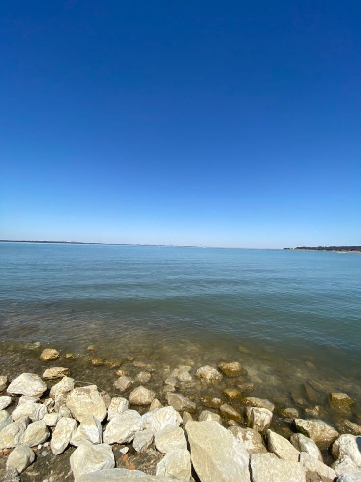 the water is crystal blue and there are rocks on the shore in front of it