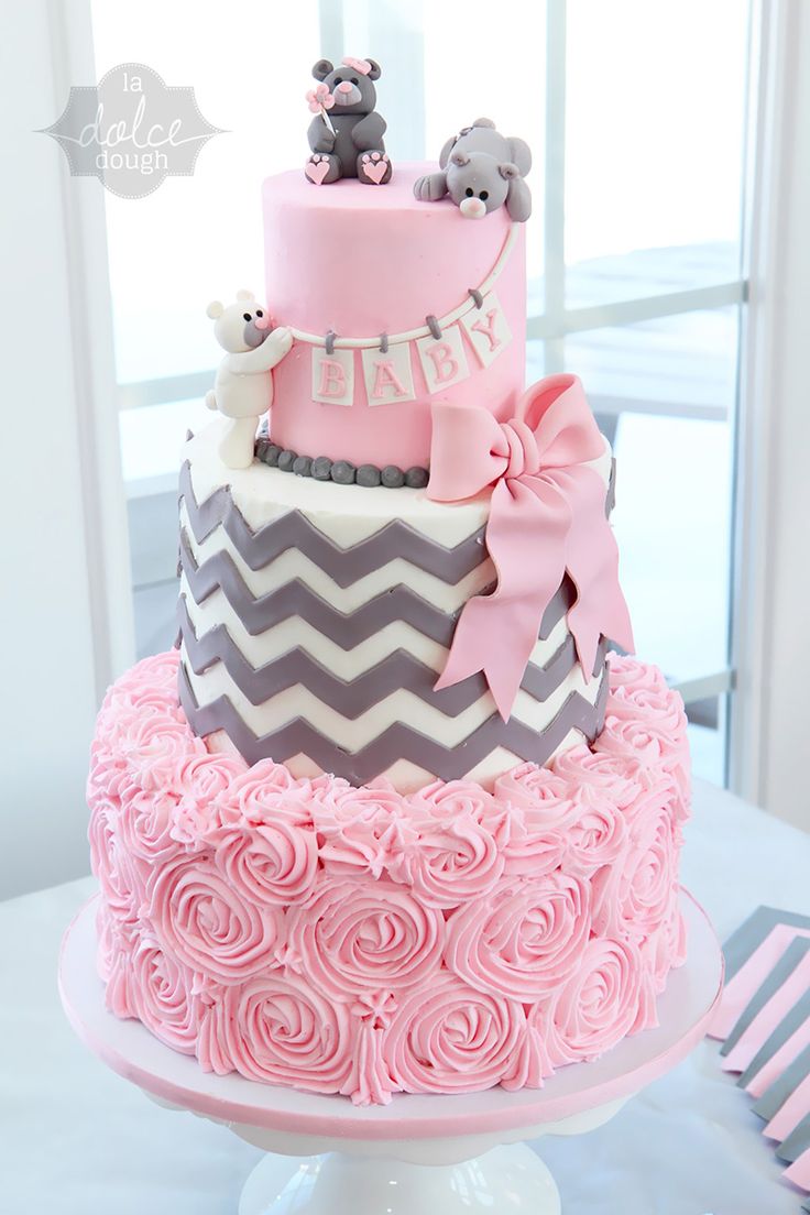 a three tiered cake with pink icing and grey chevrons on top