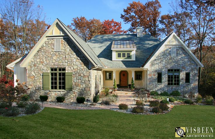 a stone house with green shutters on the front and side windows, surrounded by fall foliage