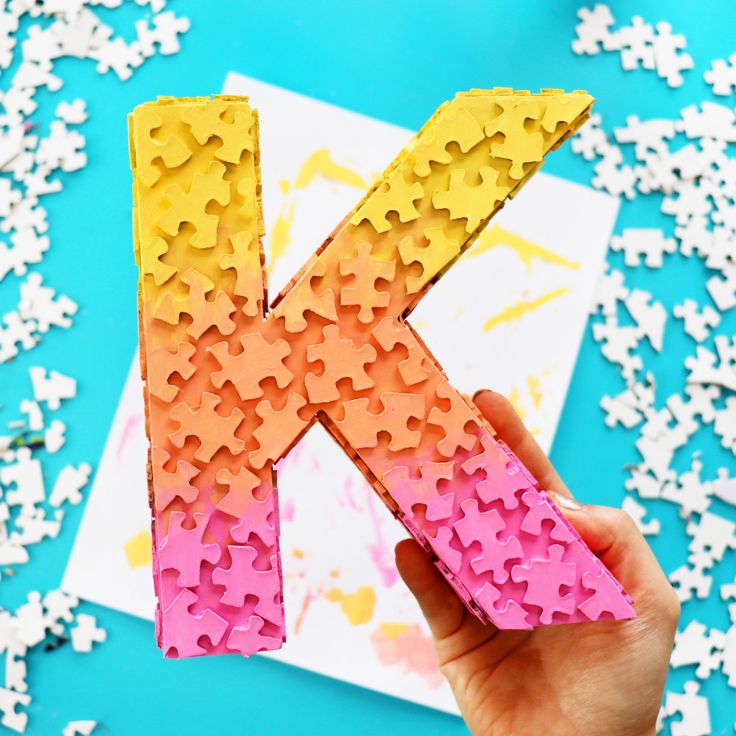 the letter k made out of puzzle pieces is shown in front of white and pink confetti