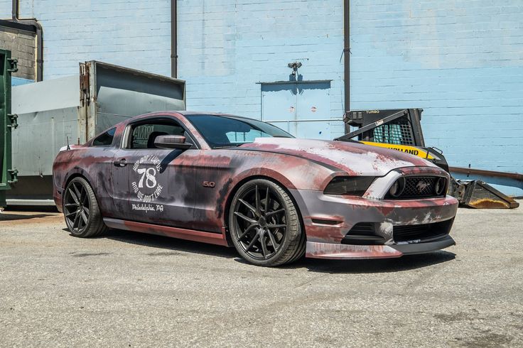 a car that is parked in front of a blue building with graffiti on the side