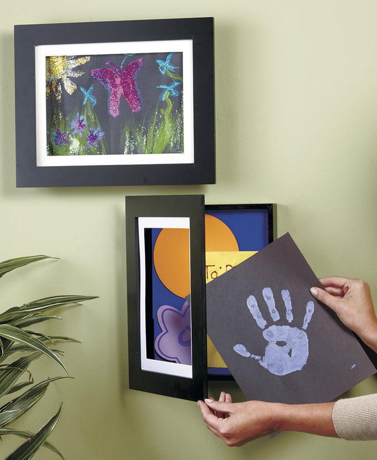 a woman is holding up some handprints in front of two framed pictures on the wall