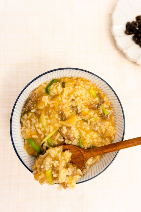 a bowl filled with rice and vegetables on top of a table next to a wooden spoon