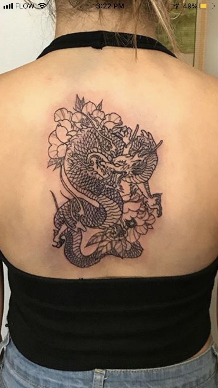 the back of a woman's shoulder with a dragon and flowers tattoo on it