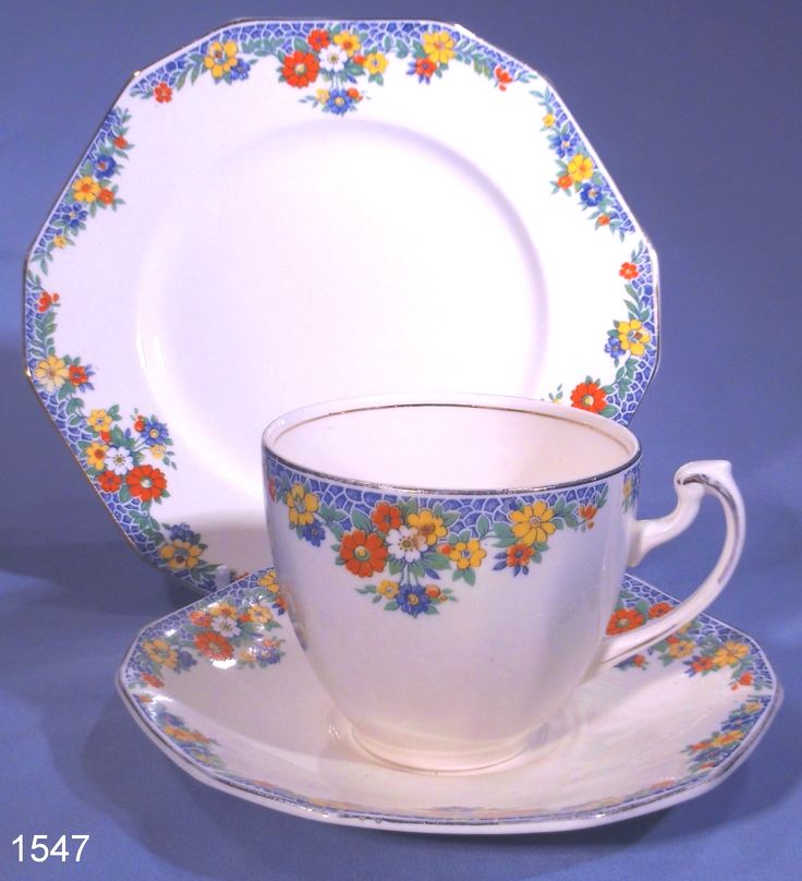 a white cup and saucer with colorful flowers on the rim is sitting in front of a blue background