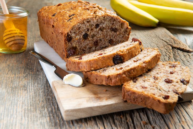 sliced loaf of banana bread sitting on top of a cutting board next to some bananas