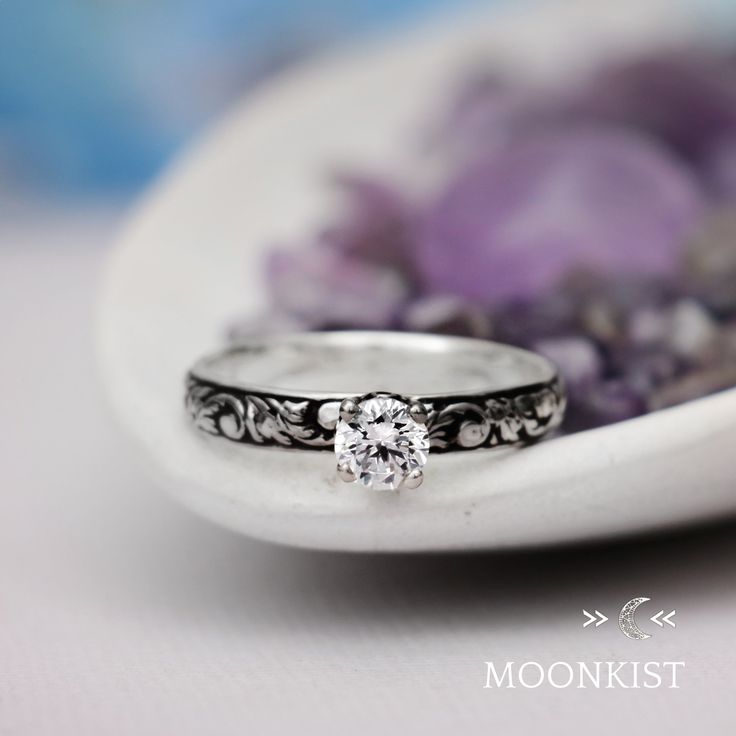 a close up of a ring on a white plate with purple flowers in the background