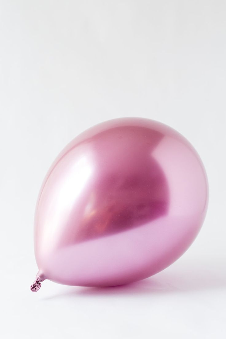 a shiny pink balloon sitting on top of a white table next to a black cat