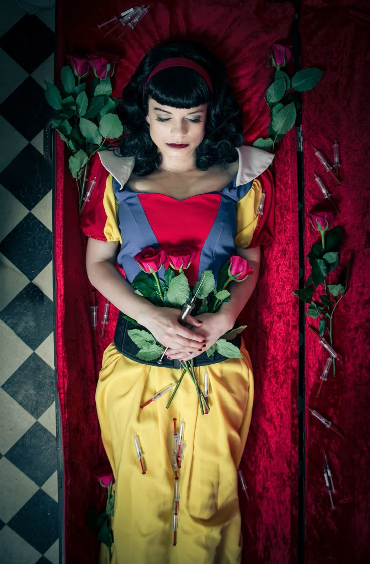 a woman laying on top of a bed with flowers in her lap and wearing a red dress