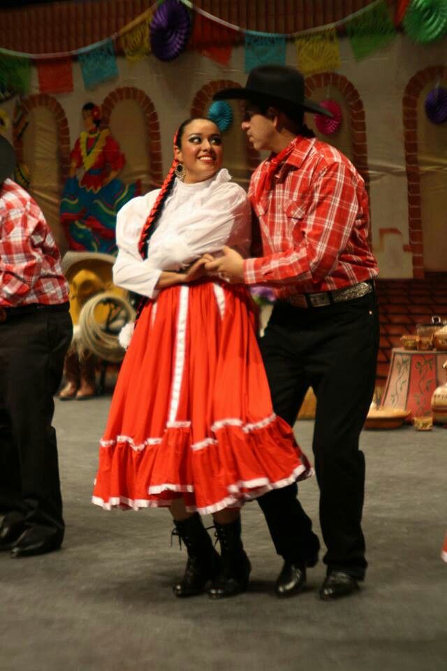 a man and woman in mexican attire dance on the stage with other people around them