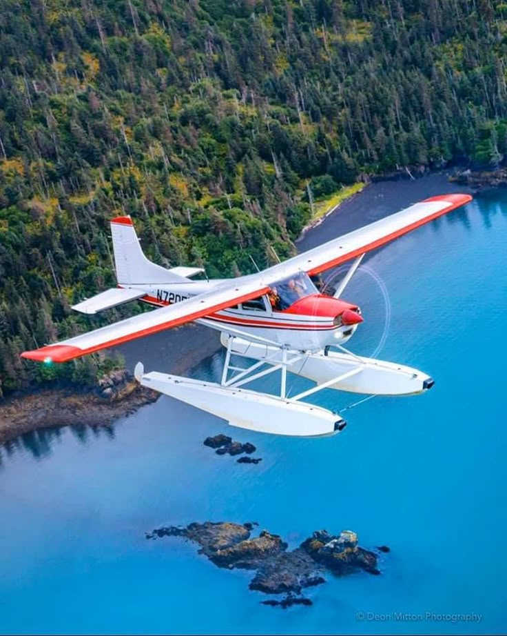 an airplane is flying over the water near some rocks and trees in the background,