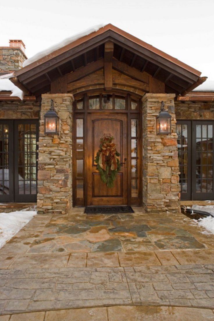 a wooden door with a wreath on it in front of a stone house covered in snow