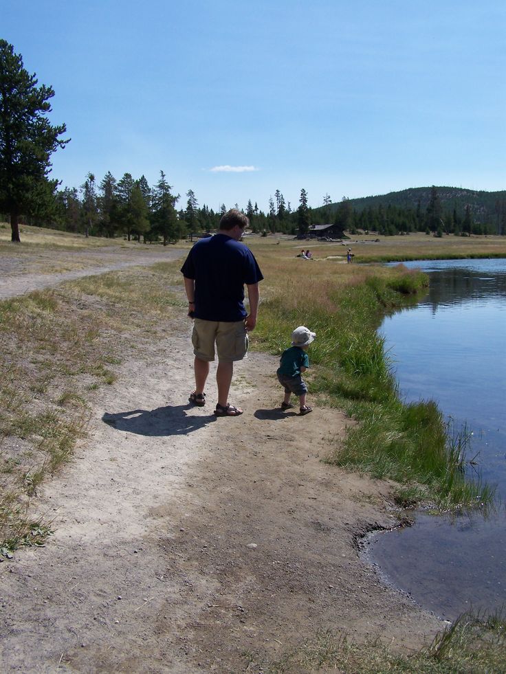 a man and his son are walking along the path near a pond in the woods