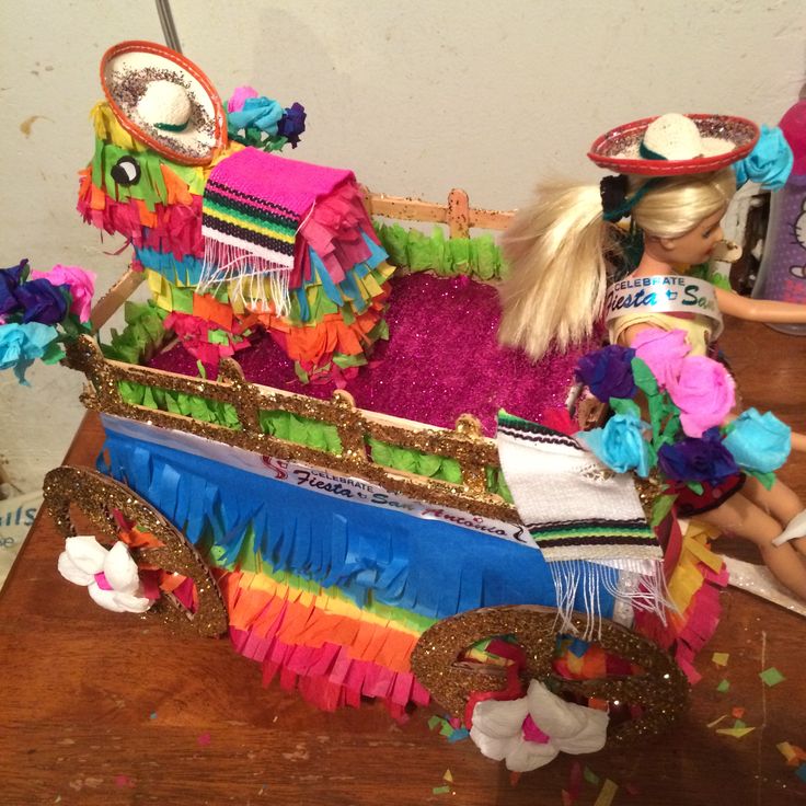 a doll sitting in a colorfully decorated carriage on a wooden table with confetti and streamers