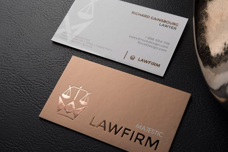 two business cards sitting next to each other on top of a black table with gold foil