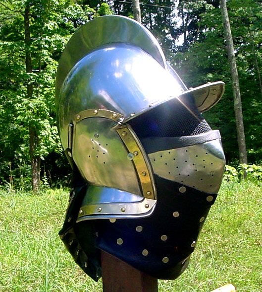 a metal helmet on top of a wooden post in the grass with trees in the background