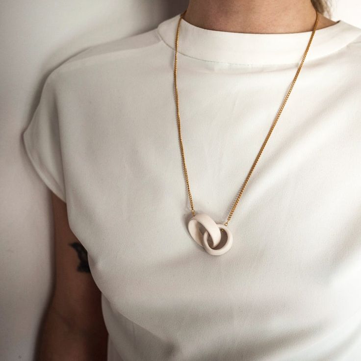 a woman wearing a white shirt and gold necklace with a heart shaped pendant on it