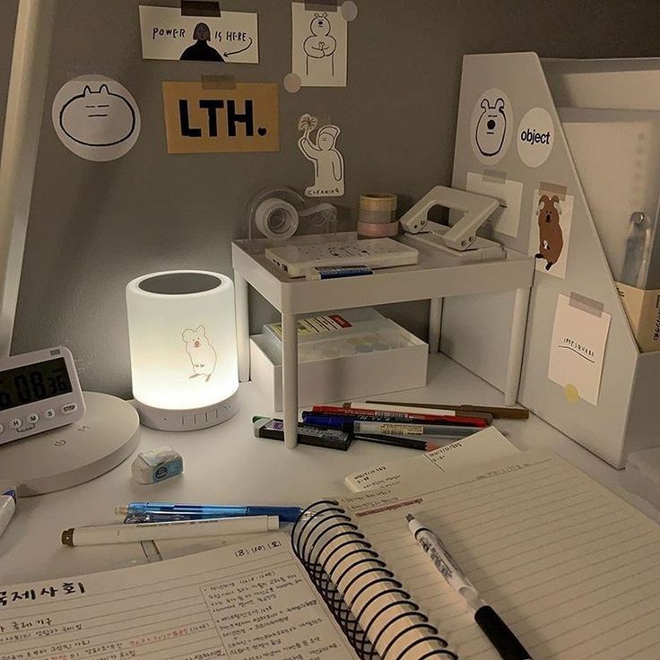 an open notebook sitting on top of a desk next to a lamp and alarm clock