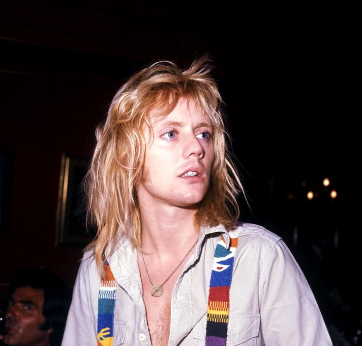 a man with long blonde hair wearing suspenders