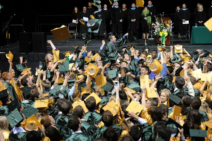 a large group of people in graduation caps and gowns with one person holding his hands up