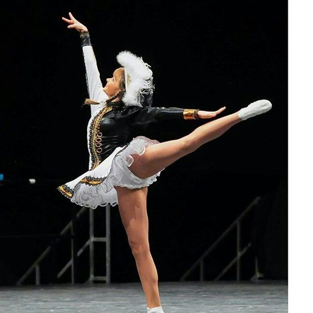 a woman in white and black outfit doing a trick on a stage with one leg up