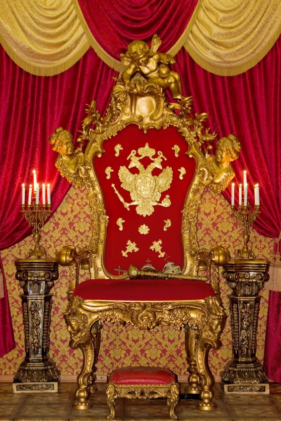 a red and gold throne sitting in front of a table with two candles on it