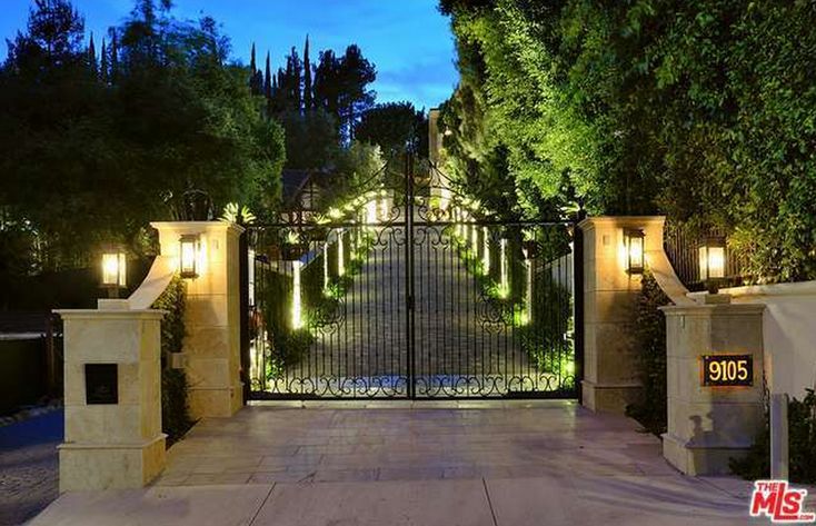 an entrance to a home with lights on the gate and trees in the background at night