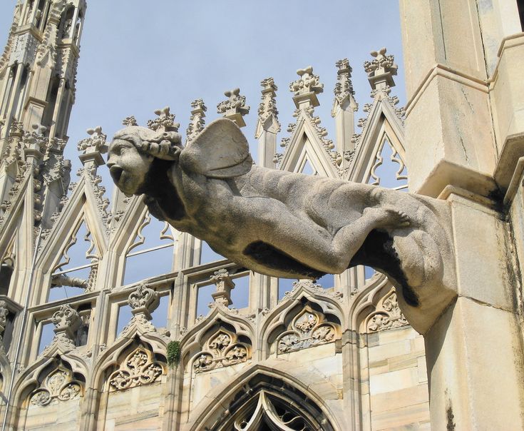 a gargoyle statue on the side of a building in front of a cathedral