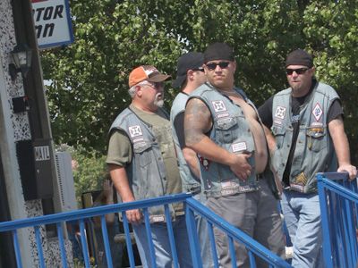 three men standing next to each other in front of a blue metal fence and some trees