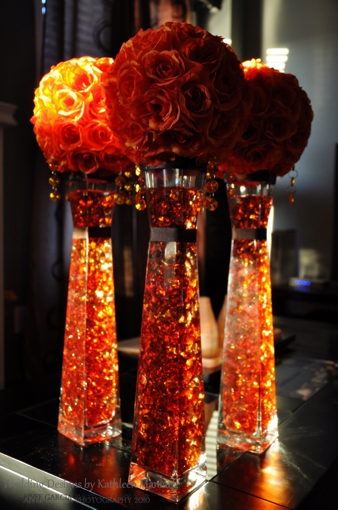 three vases filled with red flowers on top of a black table next to a mirror