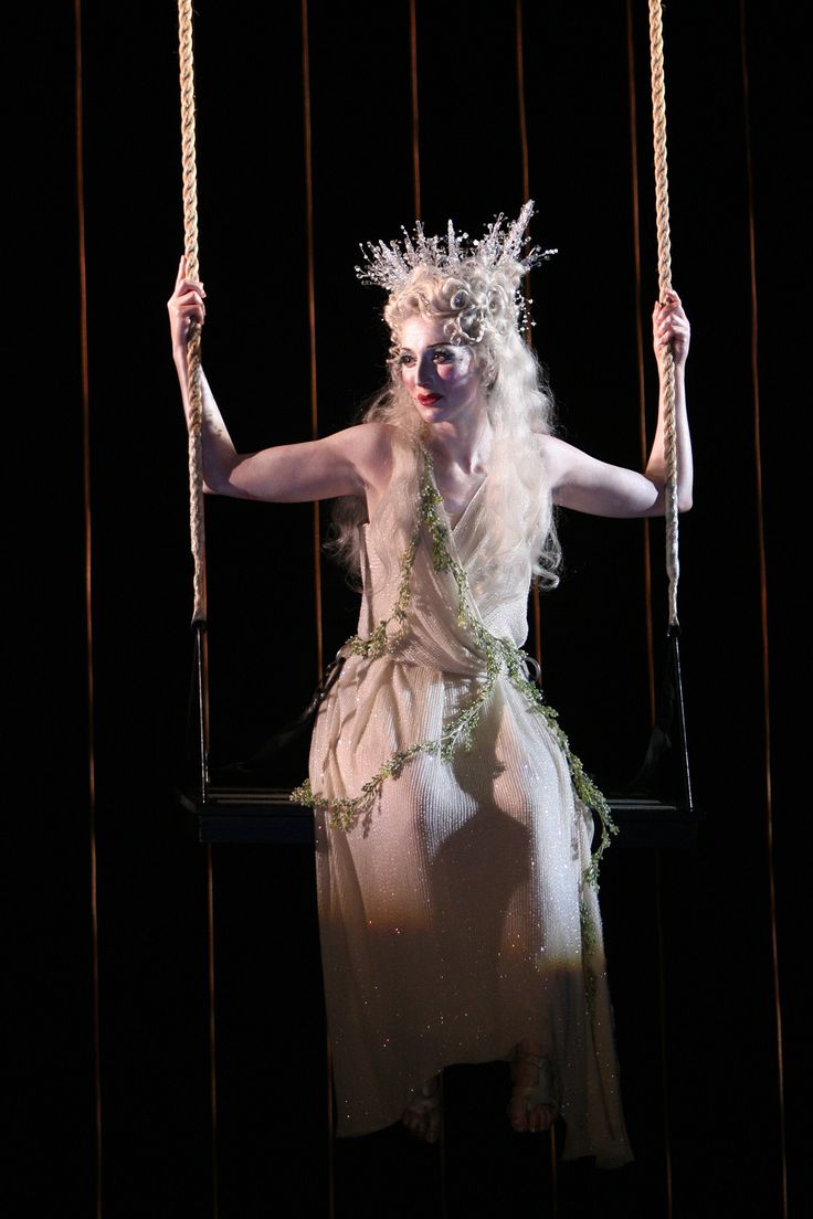 a woman with white hair and makeup is on a swing in the middle of a stage