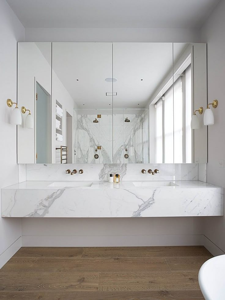 a white bathroom with marble counter tops and gold faucets on the sink area