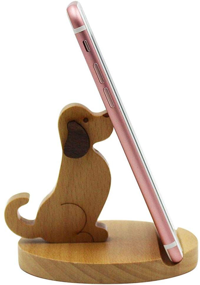 a wooden toy dog with a cell phone in it's mouth on a stand