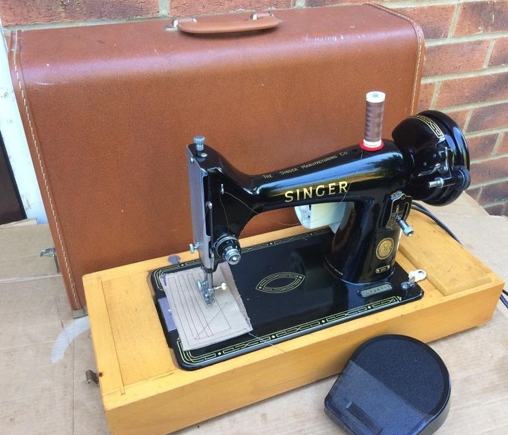 an old sewing machine sitting on top of a wooden stand next to a brown suitcase