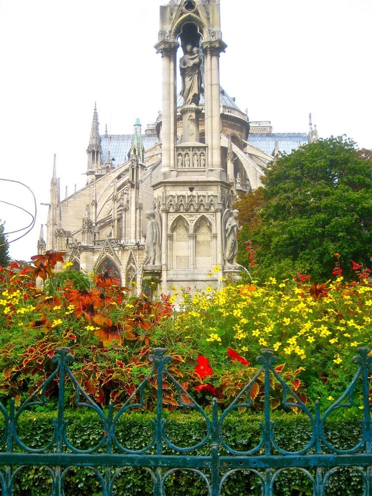 a tall building with a clock on it's face surrounded by flowers and trees