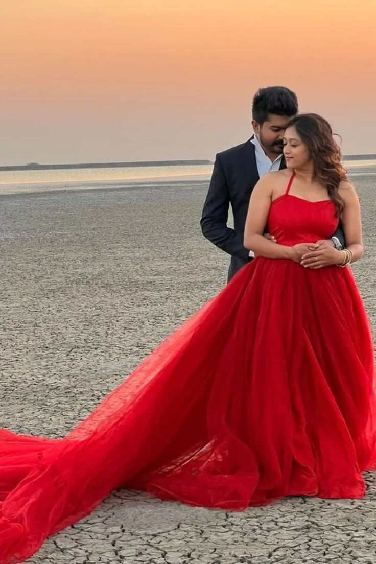 a man standing next to a woman in a red dress on top of a beach