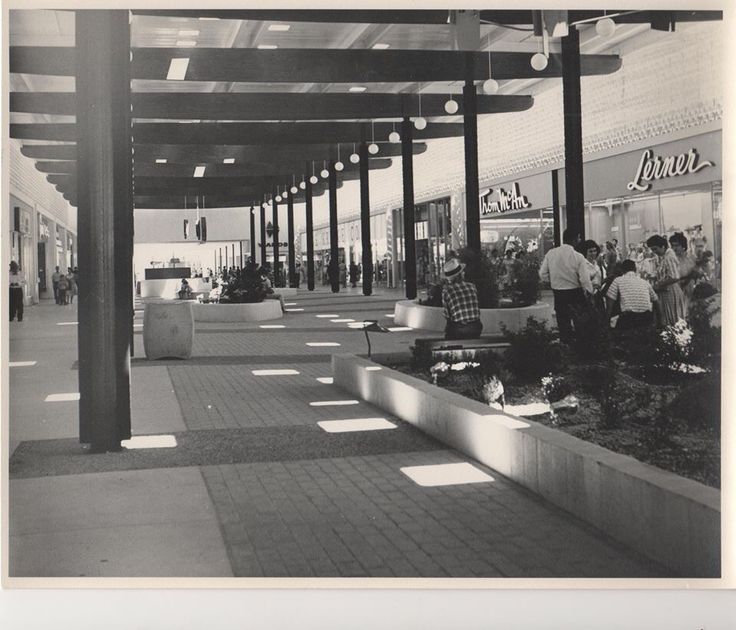 black and white photograph of people shopping in an outdoor market area with sun shining through the windows