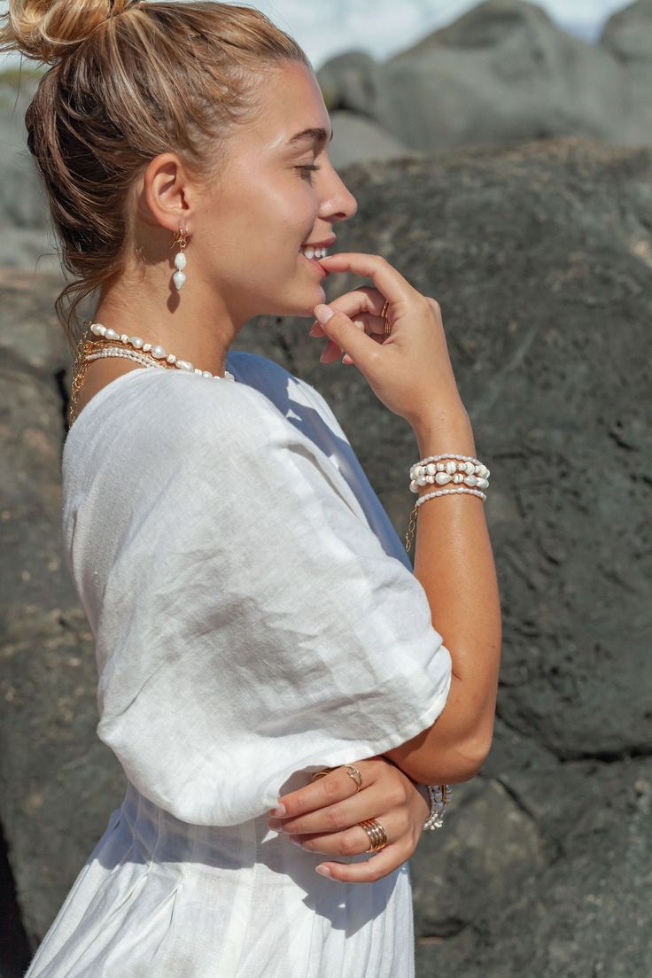 a woman standing in front of some rocks with her hand on her face and wearing bracelets