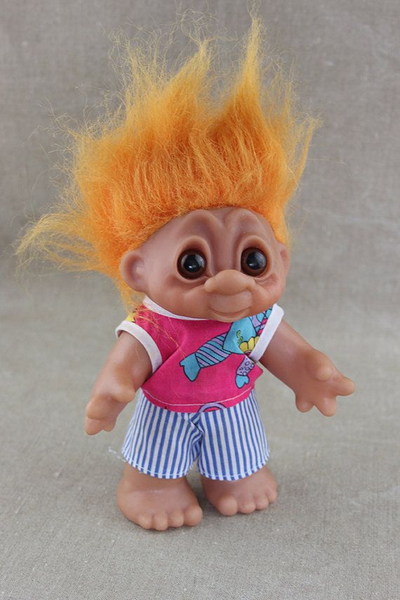 a troll doll with orange hair and blue striped shorts on it's legs, looking at the camera