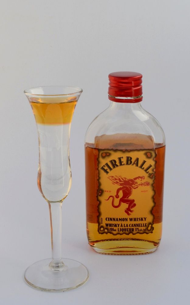 a bottle of fireball next to a glass filled with liquid on a white surface